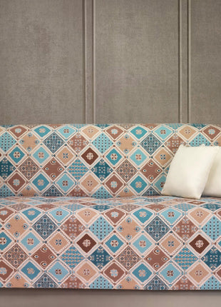 Sofabetræk LINEARE COVER MOSAICO med rombemønster i varme blå, brune og beige nuancer på sofaen.